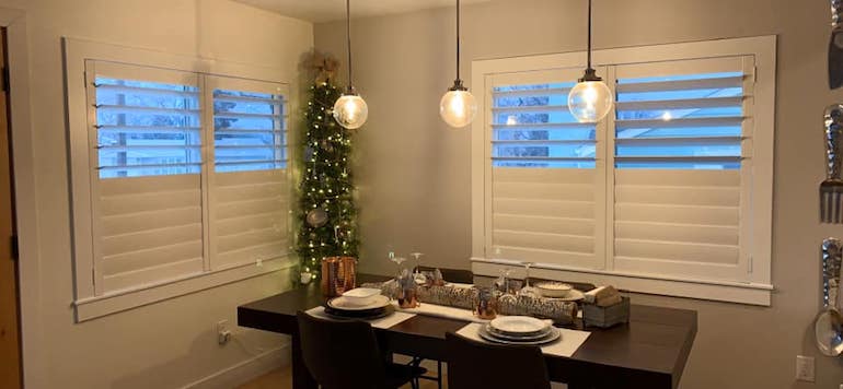 Dining room with plantation shutters and a Christmas tree. Ensuring that your lighting fixture is right for your needs should be on your holiday improvement list.